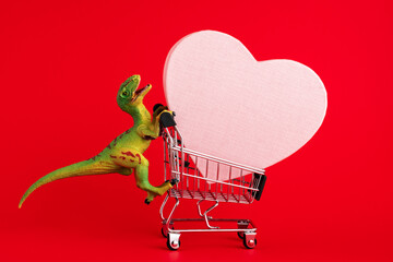 Funny green dinosaur toy with shopping cart  with big pink heart on red background. Minimal Saint...