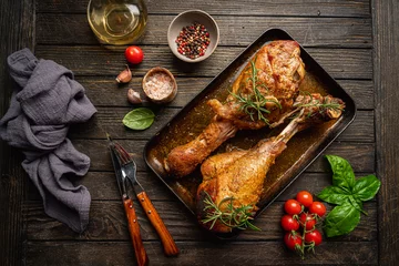 Foto op Plexiglas baked fried turkey thighs, rubbed with spices and salt on a baking sheet with garlic and rosemary on dark background, top view © petrrgoskov