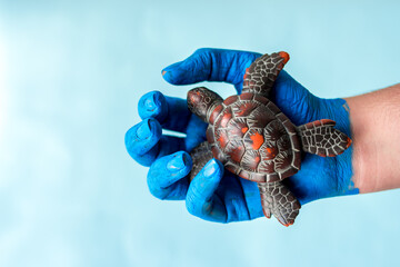 Blue painted hands holding sea turtle with blue background and copy space