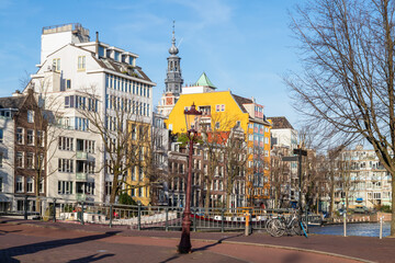 Colorful modern residential buildings along the canal with the tower of the Zuiderkerk in the center of Amsterdam in the background.