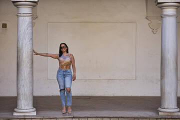 Young, beautiful, brunette and South American woman with a printed T-shirt and torn jeans, smiling and posing next to a marble column. Concept beauty, fashion, trend.