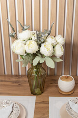 Artificial flowers for the interior. Bouquet of white peonies in a glass vase. Flowers on the dining table