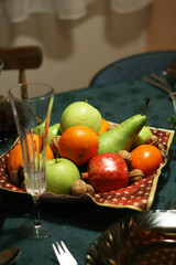 Christmas dinner table with a fruit bowl on a colorful tablecloth.