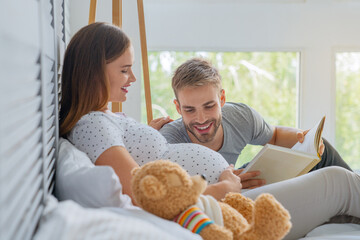 Parents lie on the couch and father read a book to child. Pregnant woman with her husband