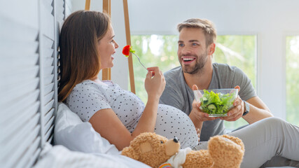 Pregnant woman eating salad with husband at home. Man take care of his wife