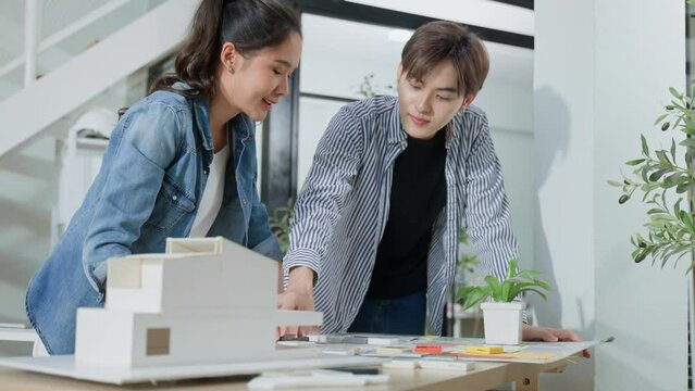 Asian architects in office discussing construction project.Young asian men and woman working together on new building model,having a discussion on a new design project,partner and blueprint in working
