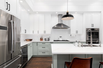 A kitchen detail with white and sage green cabinets, a large island, subway tile backsplash, and...