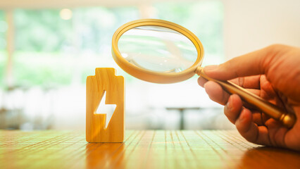 ฺBusinessman holding a magnifying glass to electric symbol .Technology battery high power...