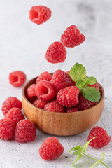 Fresh sweet raspberry falling into wooden bowl with berries and mint leaves on light grunge  stone background.