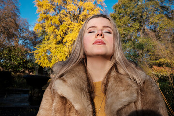 Relaxed young woman with closed eyes posing in an autumn park. - obrazy, fototapety, plakaty