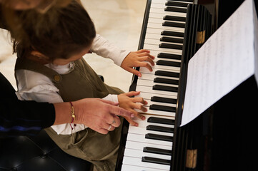 Top view music teacher, pianist holding the hands of a child girl, teaching piano lesson showing...