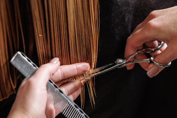 hairdresser makes a haircut to a woman in the salon. The hairdresser cuts wet hair, combing with a...