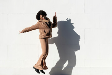 Funny young black woman jumping happily in front of white wall.