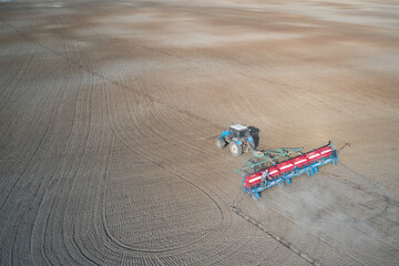 Panoramic aerial view of a field with a tractor with a trailed seeder at work. Two workers on the seeder monitor the quality of seed sowing and mineral fertilizer rationing.