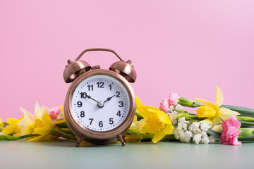Alarm clock with spring flowers. Spring time, daylight savings concept, spring forward - obrazy, fototapety, plakaty