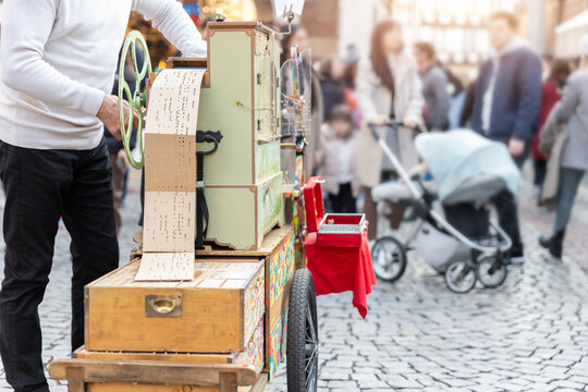 Street artist busker man playing music by organ barrel vintage wooden box machine at crowded old european city France. Person musician grinder busking with retro music instrument tool outdoors
