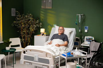 An elderly man lies in a hospital bed in a modern hospital room gaining strength after surgery.