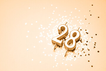 28 years celebration festive background made with golden candle in the form of number Twenty-eight lying on sparkles. Universal holiday banner with copy space.