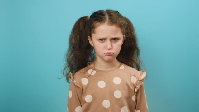 Portrait of naughty upset preteen caucasian girl sulking and grimacing expressing discontent, posing isolated over plain blue color background wall in studio. Misbehavior and childhood concept