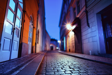 Urban alleyway at night with city lights and cobblestone pavement.