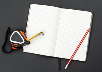 Blank notepad with measuring tape and pencil on black. Top view. Copy space. - 696068509