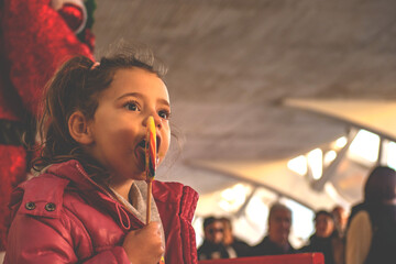 Portrait of a girl with innocent look eating a colorful popsicle on an out of focus background,...
