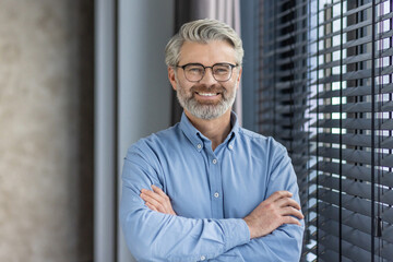 Portrait of mature successful businessman boss, senior gray-haired man inside office smiling looking at camera with crossed arms, experienced financier banker accountant in shirt. - obrazy, fototapety, plakaty