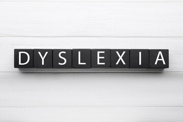 Black cubes with word Dyslexia on white wooden background, flat lay