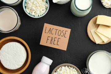 Dairy products and card with phrase Lactose free on black textured table, flat lay