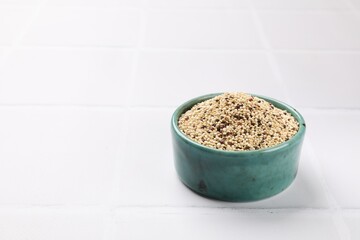 Raw quinoa seeds in bowl on white table, closeup. Space for text