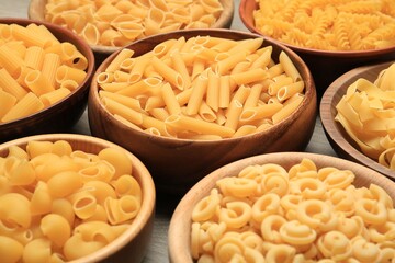 Different types of pasta in bowls on table, closeup