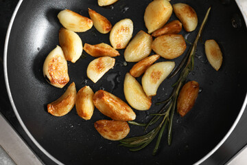 Frying pan with fried garlic cloves and rosemary, top view