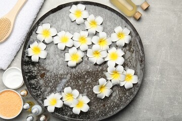 Fototapeta na wymiar Bowl of water with flowers and different spa supplies on light grey table, flat lay