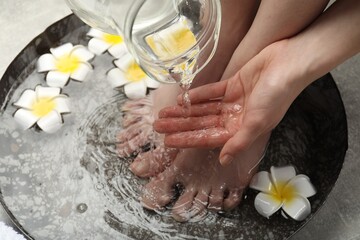 Woman pouring water onto hand while soaking her feet in bowl on floor, above view. Spa treatment