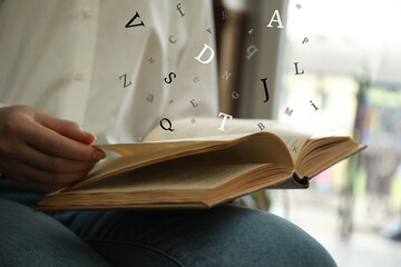 Woman reading book with letters flying over it indoors, closeup