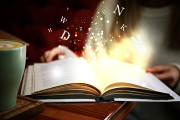 Woman reading shiny magic book with letters flying over it, closeup