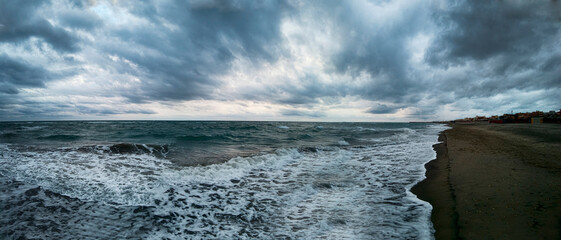 Awesome panoramic 180 degrees of rough sea at sunset on blue hour at  beach, a dramatic sky with amazing light and cloudscape and sun reflections with on water edge crashing with foam