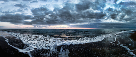 Stunning panoramic 180 degrees of rough sea at sunset on blue hour at  beach, a dramatic sky with amazing light and cloudscape and sun reflections with on water edge crashing with foam