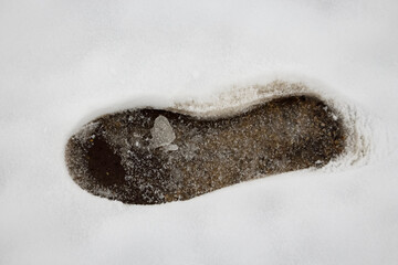 Big boot footprint in fresh wet white snow showing transparent dark ice and some frozen grass under it