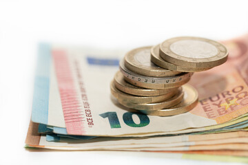 Close-up of several euro notes stacked on top of each other. Euro coins lie on top. The background is light-coloured.