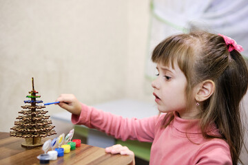 A little girl paints a wooden toy in the shape of a Christmas tree. She works on her masterpiece...