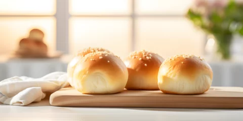 Tuinposter Close up of fresh baked dinner roll buns on a kitchen table, blurry blight background  © TatjanaMeininger