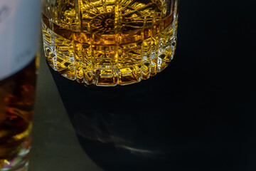 Bottle and glass with luxury spirit drink gold color close-up on dark background with shadows