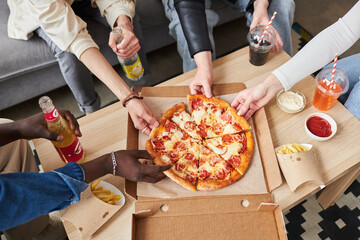 Top down view of people hands sharing delicious pepperoni pizza and drinking lemonades at home party while sitting at table