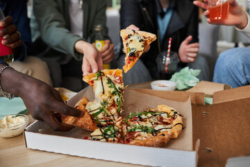 Close up shot of multi-ethnic peoples hands taking pieces of delicious pizza with sauce and greens...