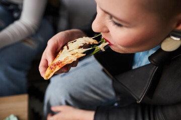 Close up shot of young girl biting delicious slice of pizza with cheese stretching from her mouth,...