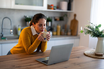 Smiling businesswoman having a break and drinking tea in front of laptop at desk. Young woman...