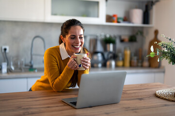 Smiling businesswoman having tea while discussing over video call on laptop at desk in home office.