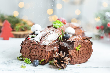 Traditional  French Christmas chocolate dessert  BûchedeNoël (Yule log). Christmas festive pastry in the shape of a log on the white background with blurred bokeh lights