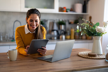 Female business person using digital tablet and laptop e-learning or remote working at home office, looking at tablet watching webinar, learning training, studying online seminar or video calling.